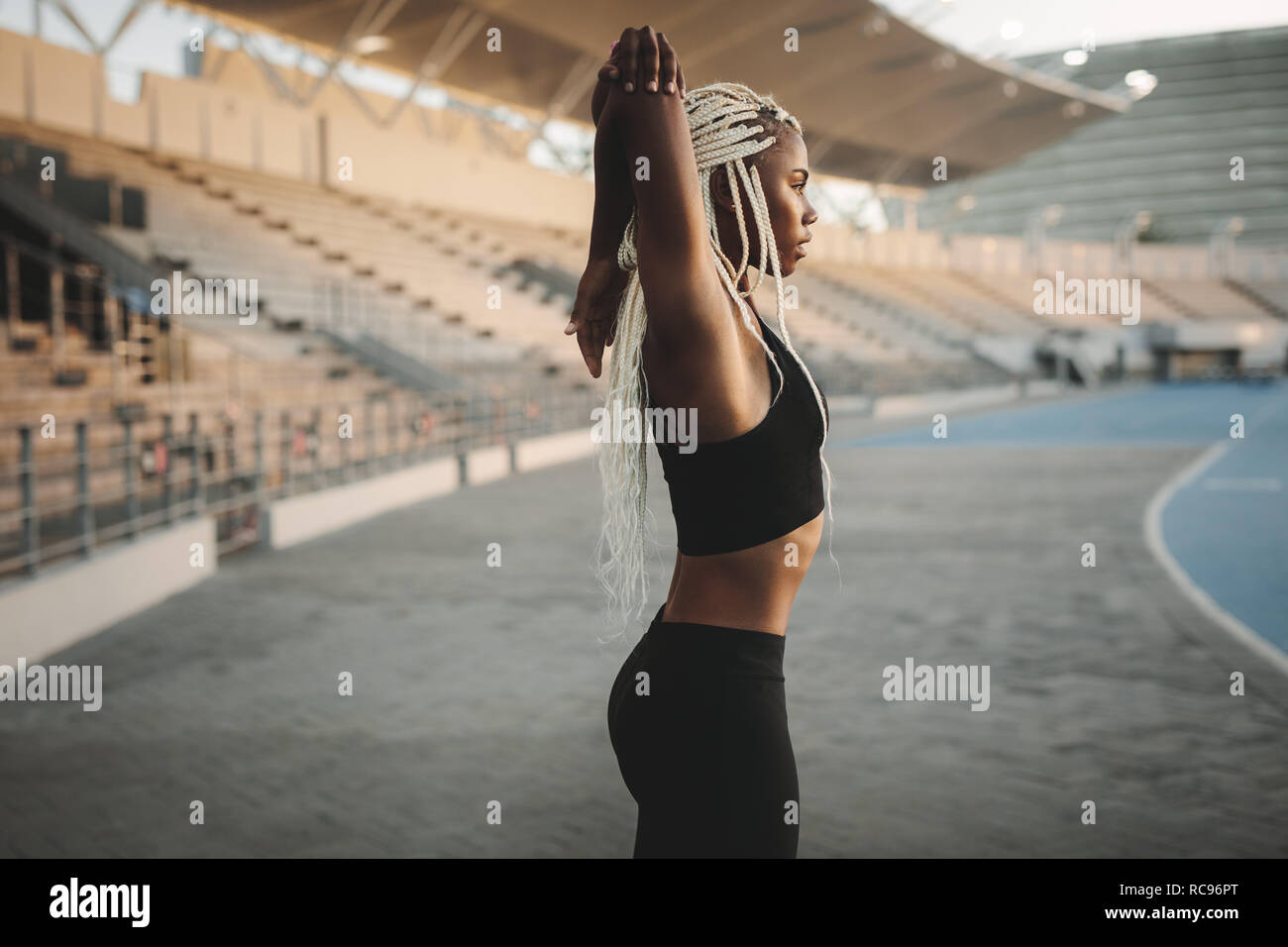Woman athlete doing exercise in a track and field stadium. Runner warming up stretching hands and shoulders before running. Stock Photo