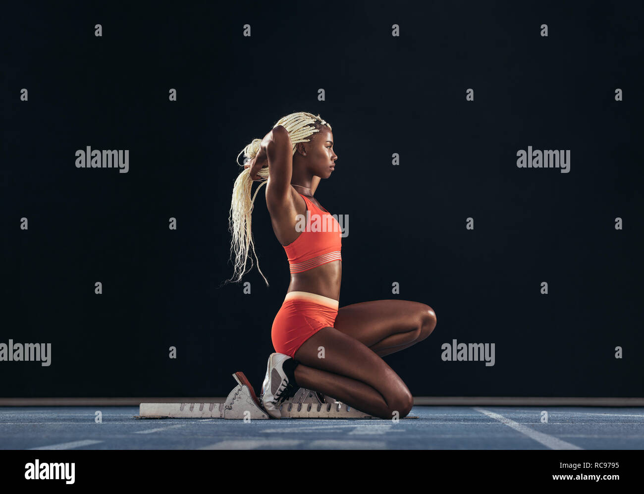 Female sprinter sitting at the start line near starting block on a ...