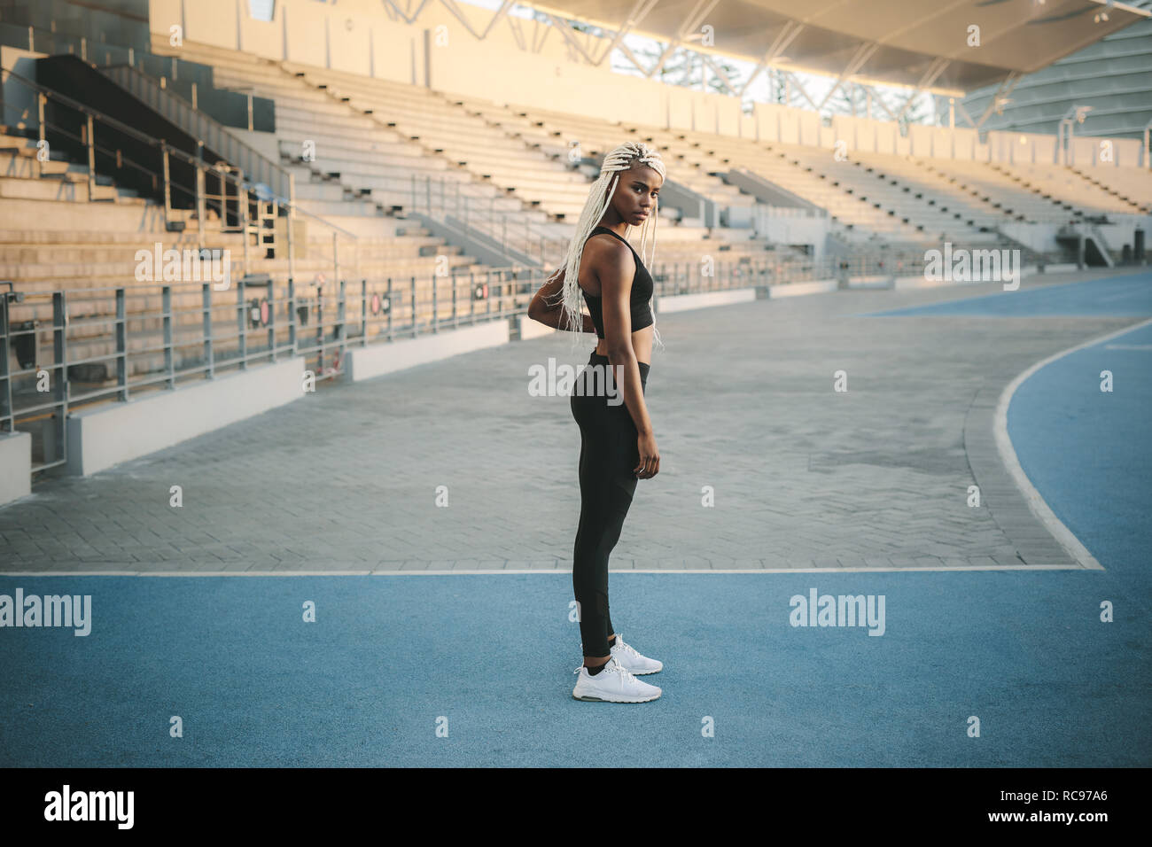 Female athlete standing inside a track and field stadium ready. Female runner getting ready to warm up and workout before running. Stock Photo
