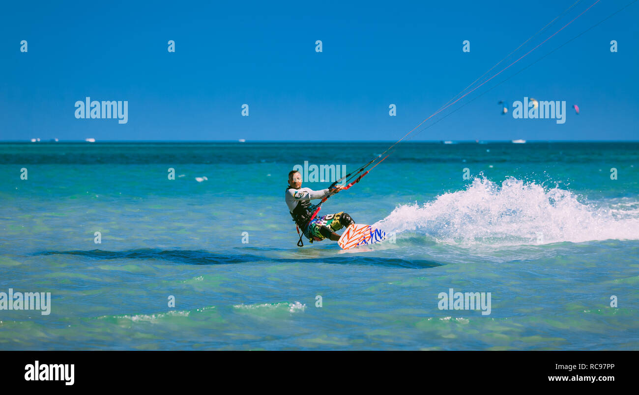 Egypt, Hurghada - 30 November, 2017: The kitesurfer gliding on the Red sea waves. Extreme outdoor activity. The lone man in the sport equipment riding on the water surface. Stunning marine scene. Stock Photo