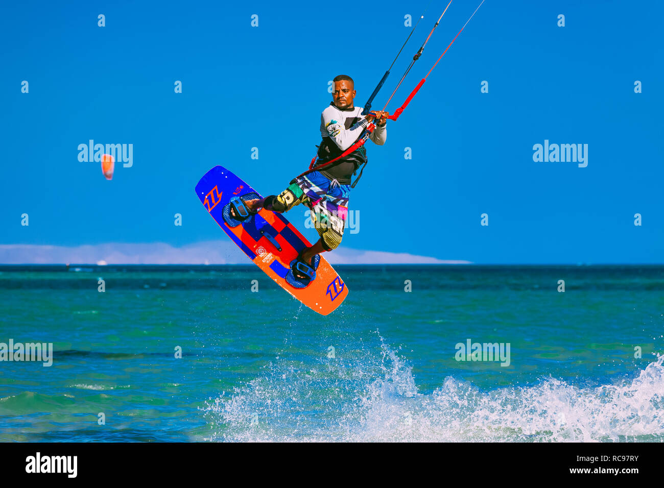 Egypt, Hurghada - 30 November, 2017: The kitesurfer soaring in the blue sky over the Red sea surface. Amazing wave splash. The extreme water sport activity. Popular tourist attraction. Stock Photo