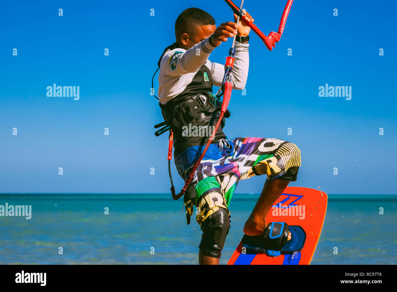 Egypt, Hurghada - 30 November, 2017: Close-up side view of kitesurfer standing on the wakeboard holding the kite straps. Amazing Red sea and the blue sky background. The professional kitesurfing. Stock Photo