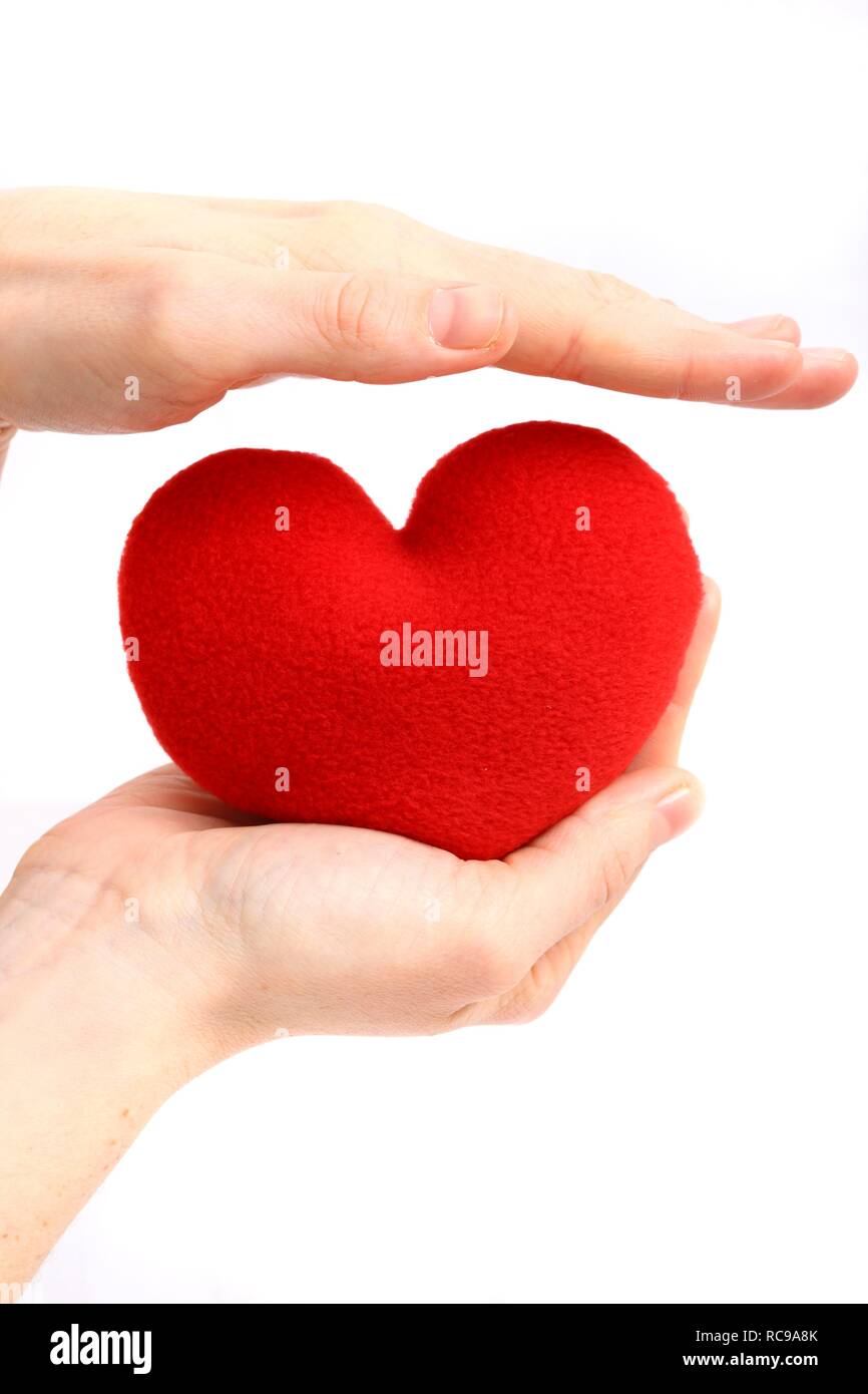 Hand being held protectively above a red heart, symbolic image for heart disease, heart attack, a diseased heart, cardiology Stock Photo
