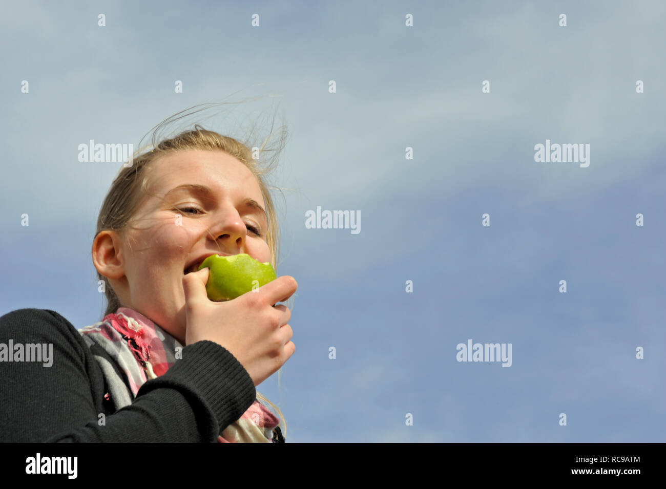 junge Frau beisst in einen grünen Apfel - in den sauren Apfel beissen | young woman eats a green apple - to swallow a bitter pill or to grasp the natt Stock Photo