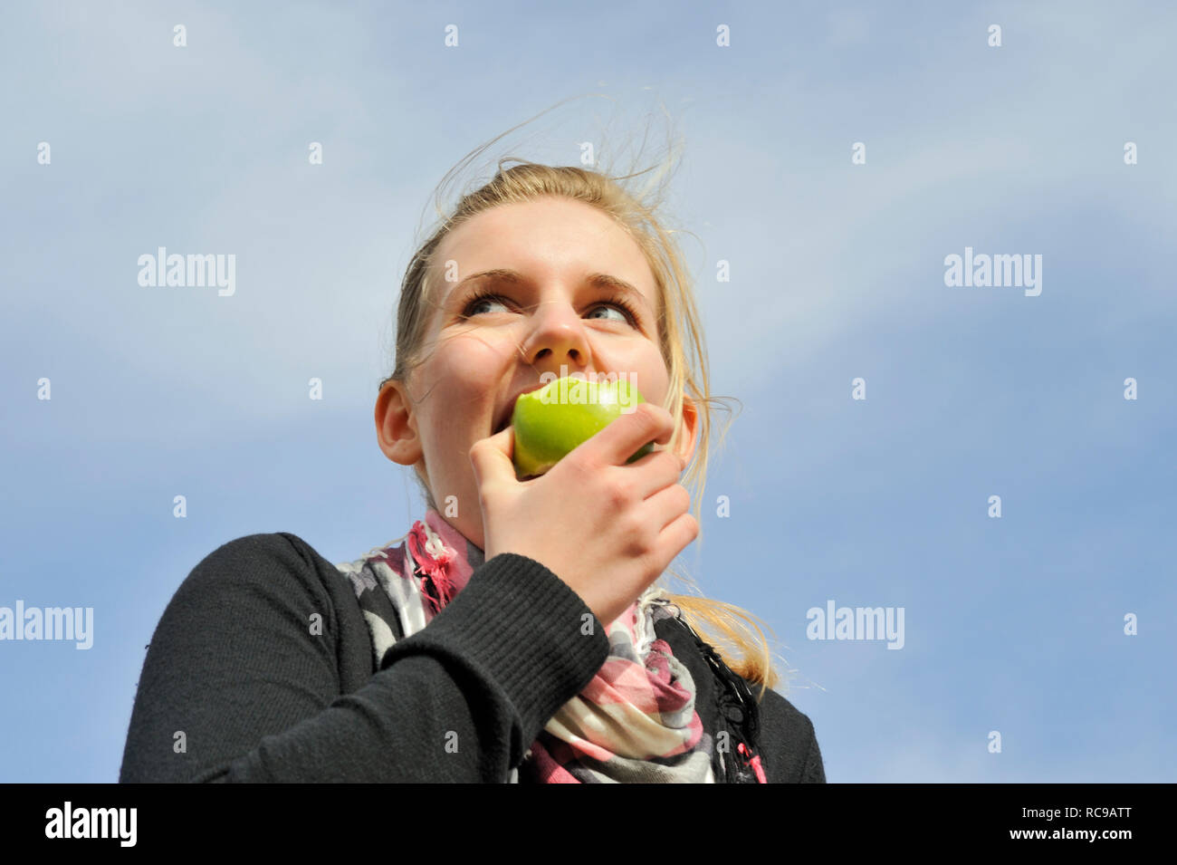 junge Frau beisst in einen grünen Apfel - in den sauren Apfel beissen | young woman eats a green apple - to swallow a bitter pill or to grasp the natt Stock Photo