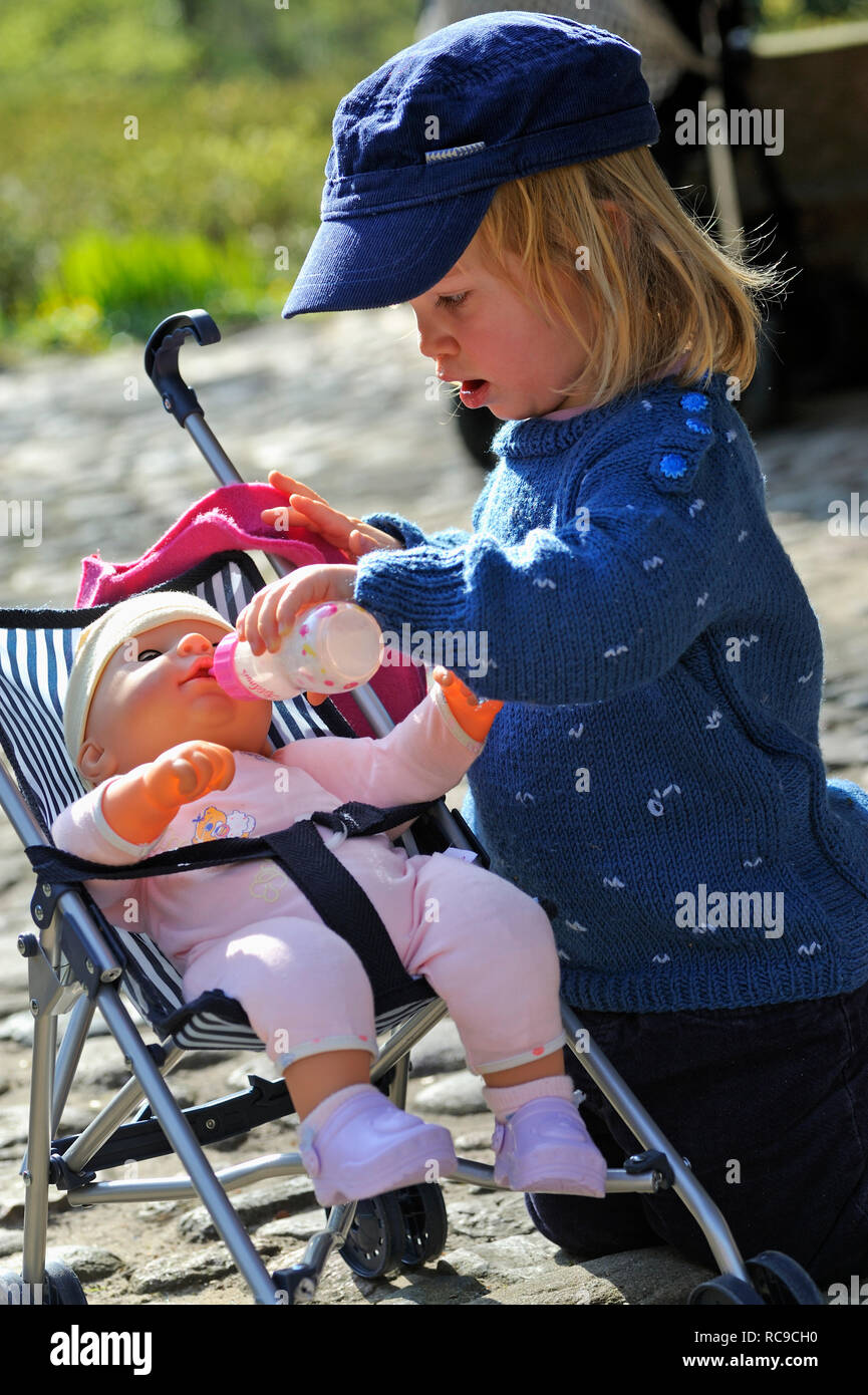 kleines Mädchen, 2 Jahre alt, kümmert sich um ihre Puppe im Puppenbuggy | little girl, 2 years old, taking care of her doll Stock Photo