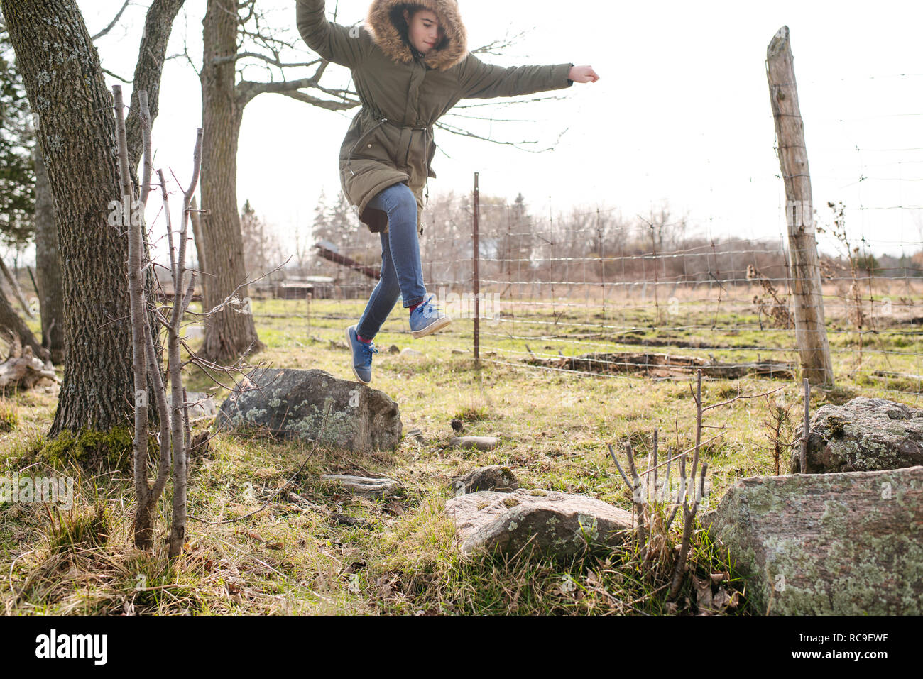 Girl jumping from rock to rock in field Stock Photo