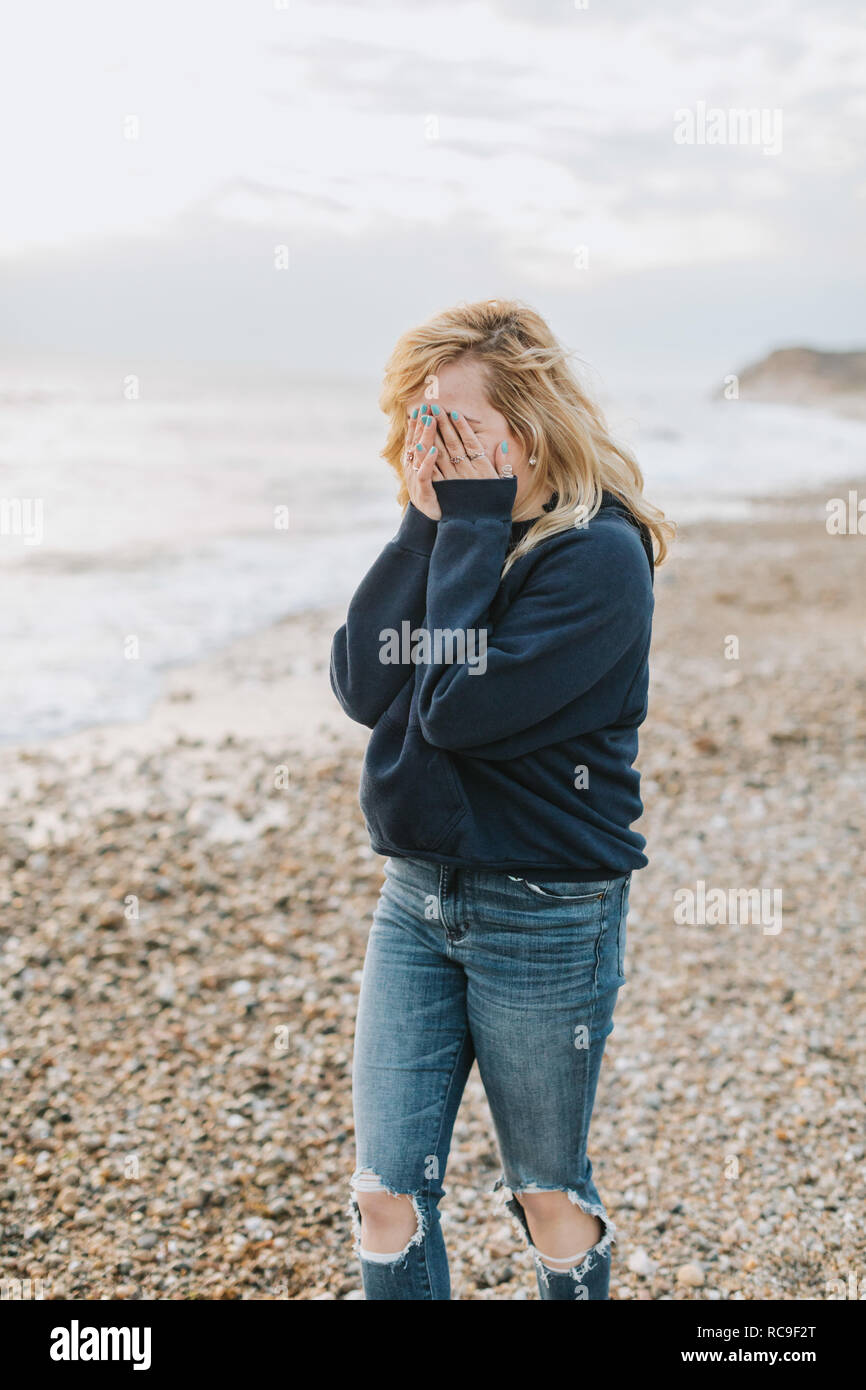 Young woman covering her face with hands on beach, Menemsha, Martha's Vineyard, Massachusetts, USA Stock Photo