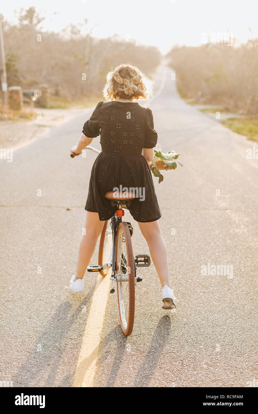 Young woman riding bicycle on rural road, rear view, Menemsha, Martha's Vineyard, Massachusetts, USA Stock Photo