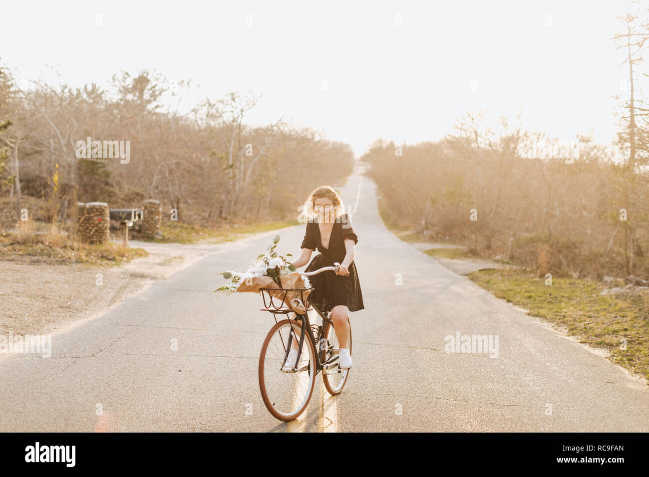 Young woman riding bicycle on rural road, Menemsha, Martha's Vineyard, Massachusetts, USA Stock Photo
