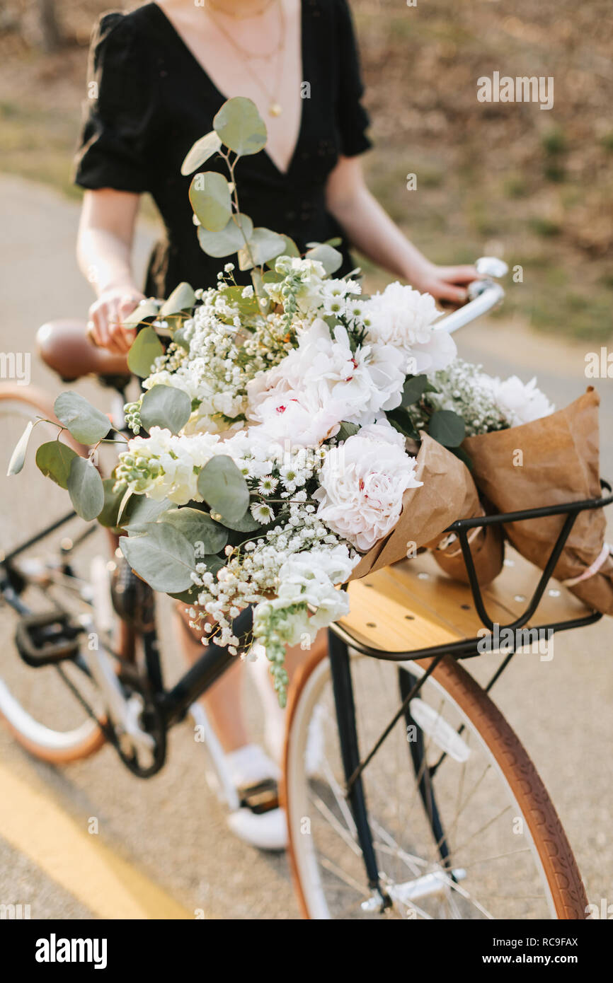 Young woman pushing bicycle with bunch of flowers on rural road, neck down, Menemsha, Martha's Vineyard, Massachusetts, USA Stock Photo