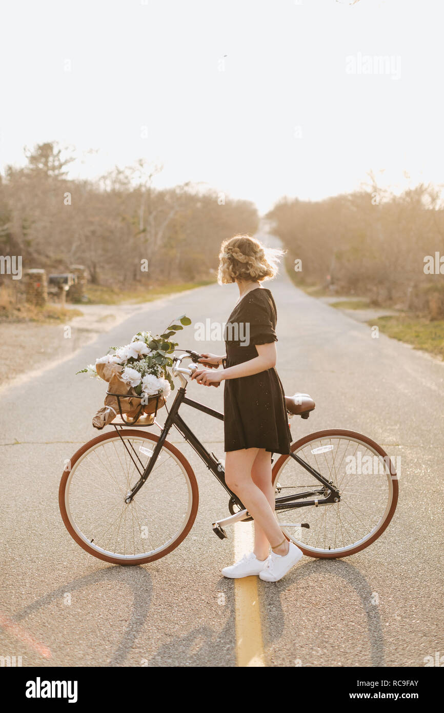 Young woman with bicycle looking sideways on rural road, Menemsha, Martha's Vineyard, Massachusetts, USA Stock Photo