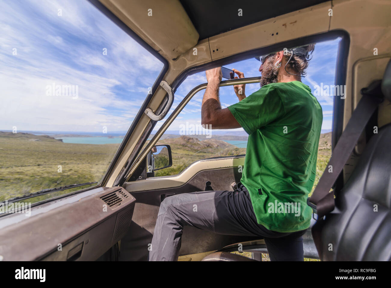 Man standing half out of car door photographing view Stock Photo