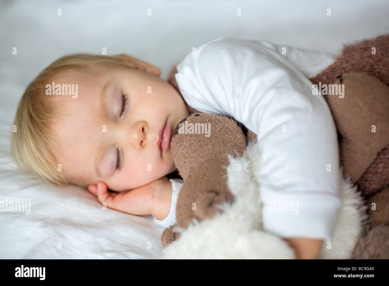 Sweet baby boy in cute overall, sleeping in bed with teddy bear stuffed  toys, winter landscape behind him Stock Photo - Alamy