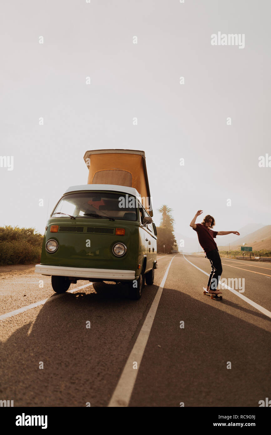 Man on road trip skateboarding by van, Ventura, California, US Stock Photo