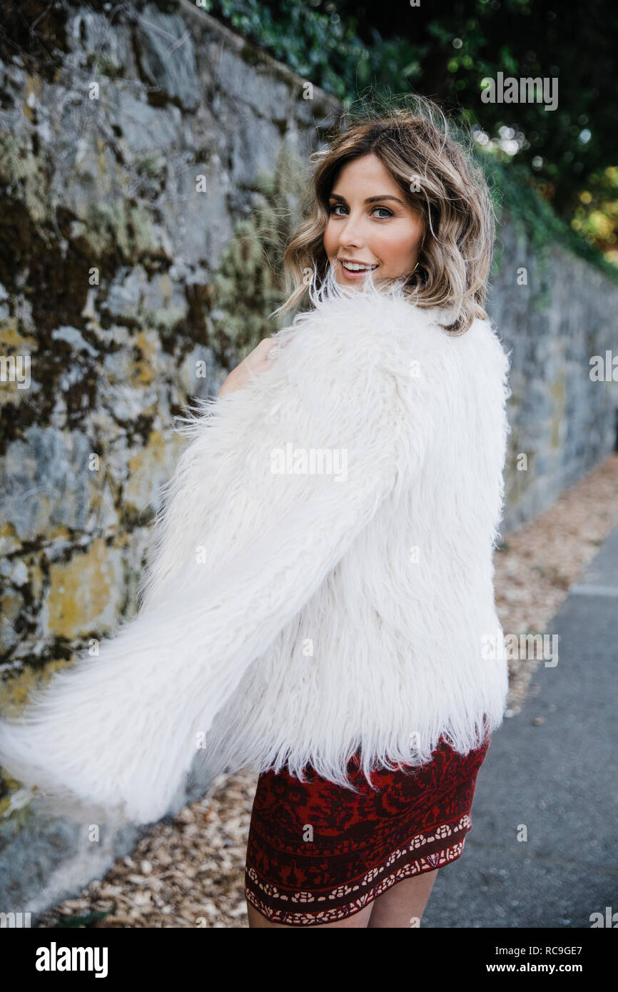 Fashionable woman walking along old stone wall, San Rafael, California, US Stock Photo