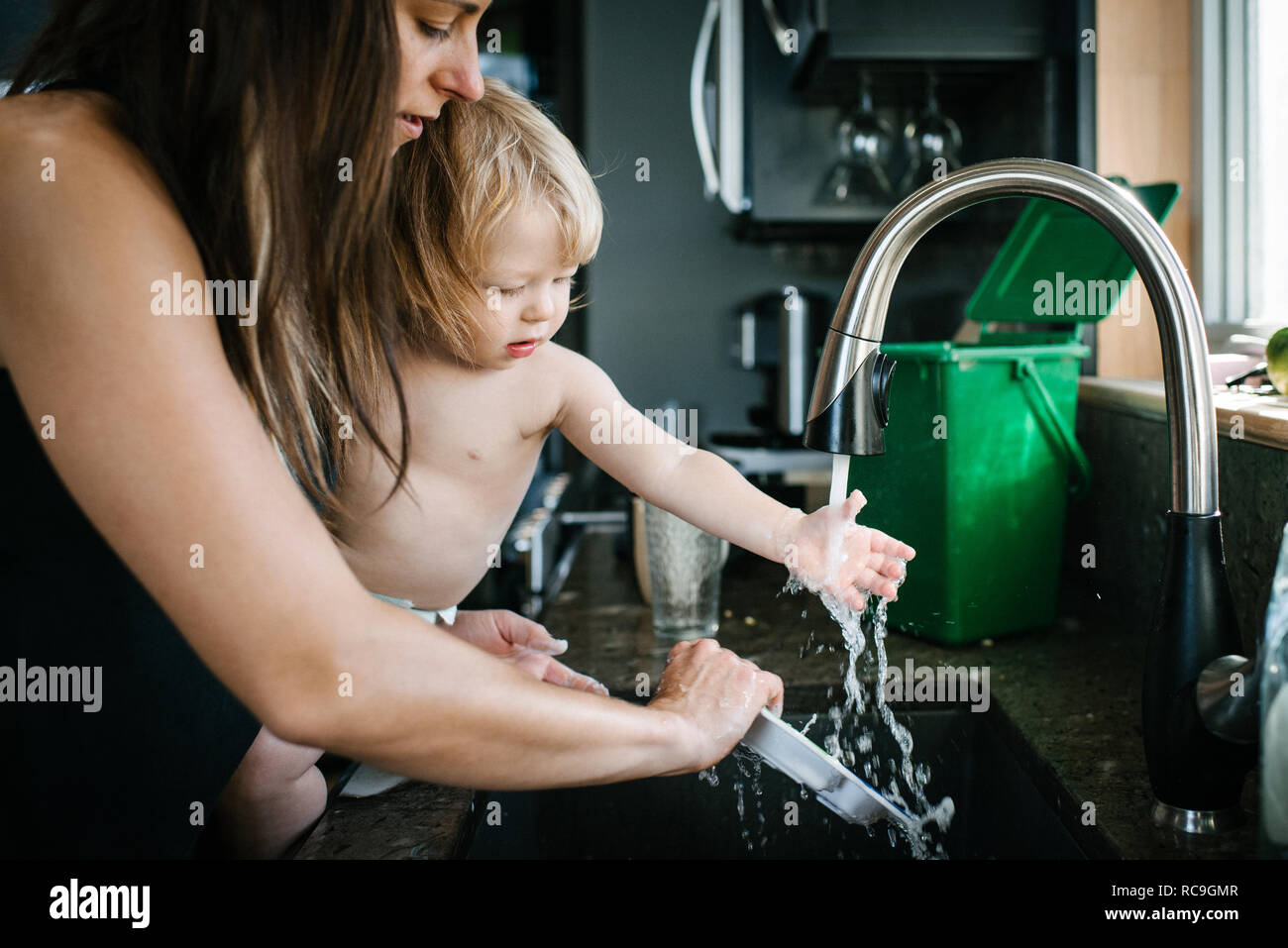Mother and son washing plate in kitchen sink Stock Photo