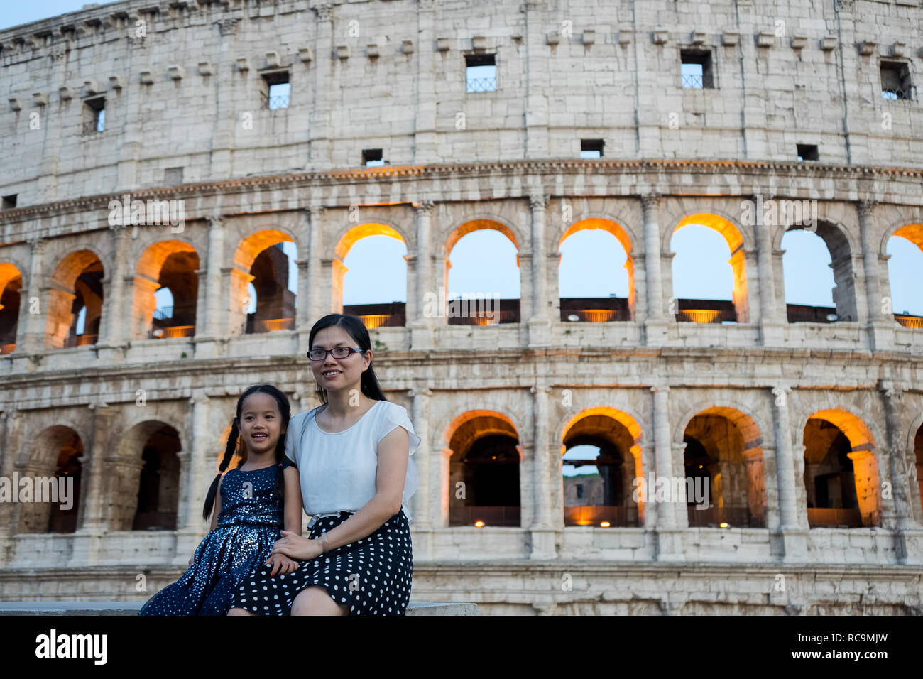 Rome, Italy, 07/27/2018: mother and daughter, Korean turists, are photographed with the illuminated Colosseum behind them. Stock Photo