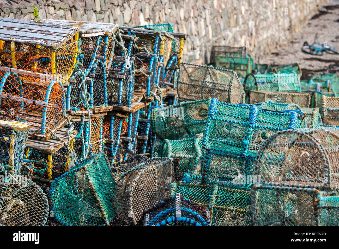 Lobster pots / prawn creels stacked against harbour wall in Plockton, Scottish Highlands, Scotland, UK Stock Photo