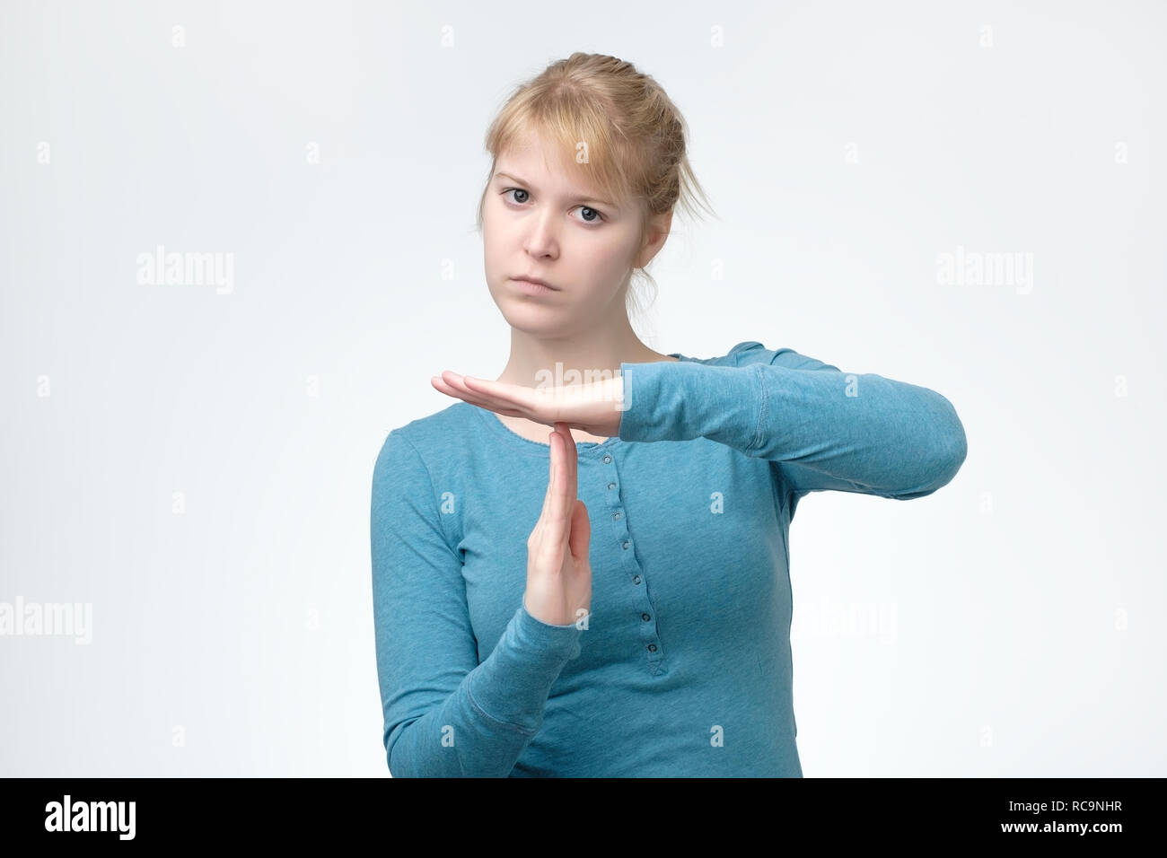 Beautiful woman in blue shirt showing time out sign over gray background Stock Photo