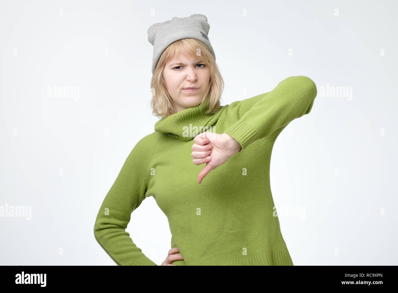 Pretty girl in green sweater and hat doing a bad signal turning thumb down over white background Stock Photo