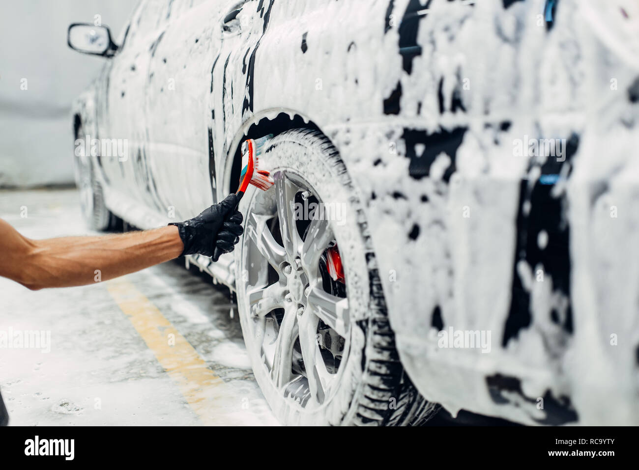 Carwash service, car in foam, side view. Auto detailing, washing of wheels  with brush Stock Photo - Alamy