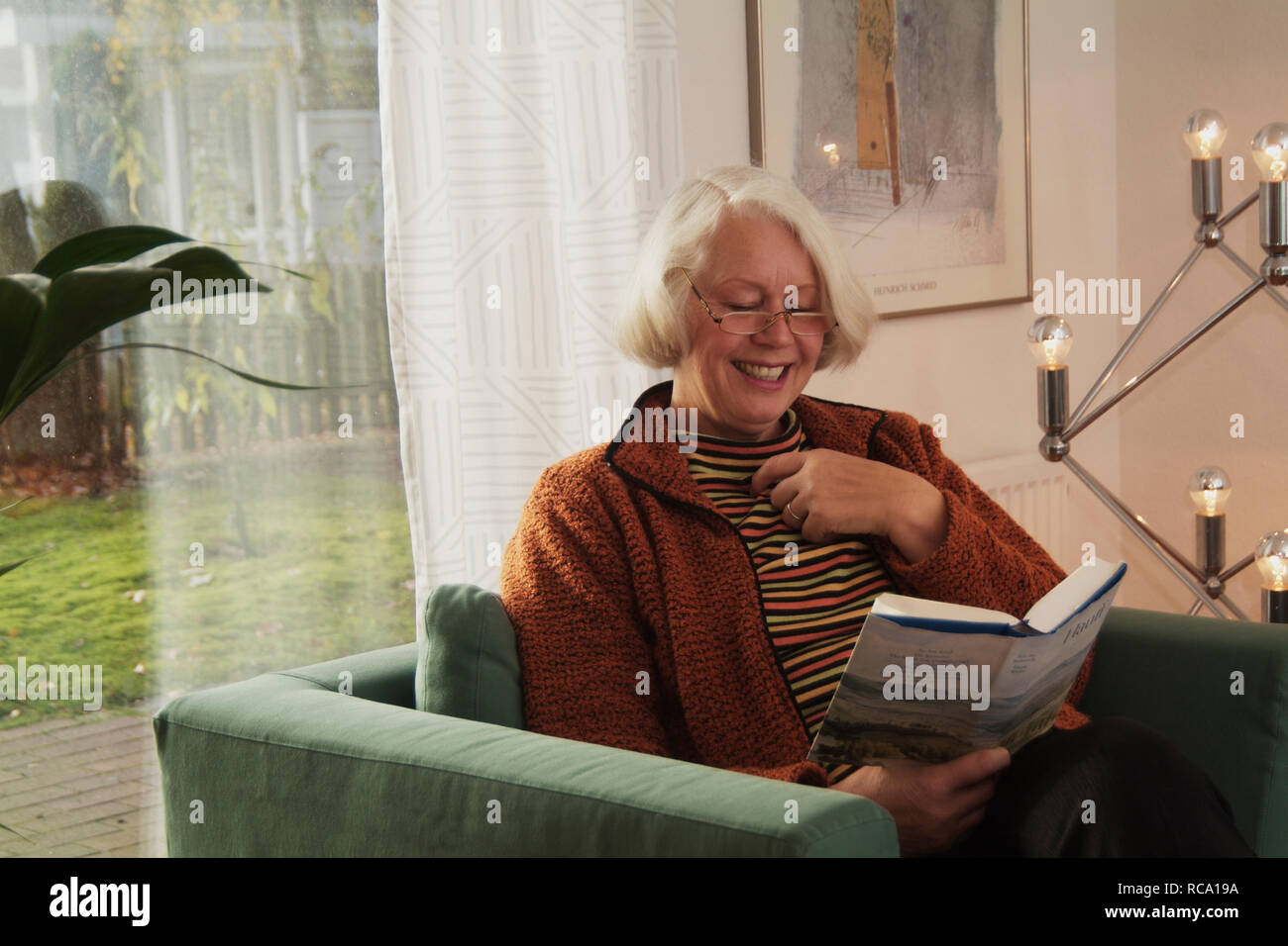 Frau mittleren Alters liest Buch auf einem Sofa | middleaged woman is reading a book on a couch Stock Photo
