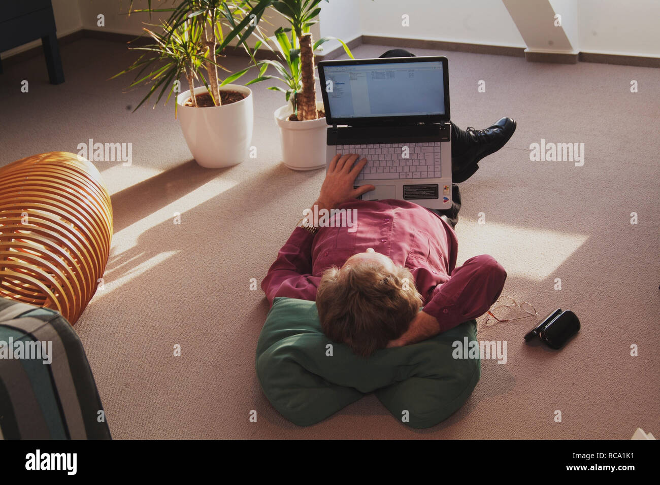 Mann mittleren Alters mit Notebook auf dem Boden liegend | middleaged man is lying on the floor with a notebook Stock Photo