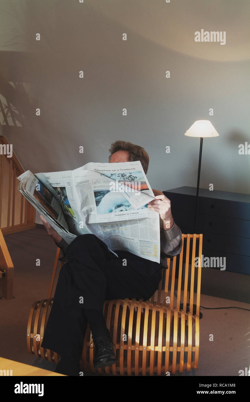 Mann mittleren Alters liest Zeitung auf einem Stuhl | middleaged man is reading a newspaper on a chair Stock Photo