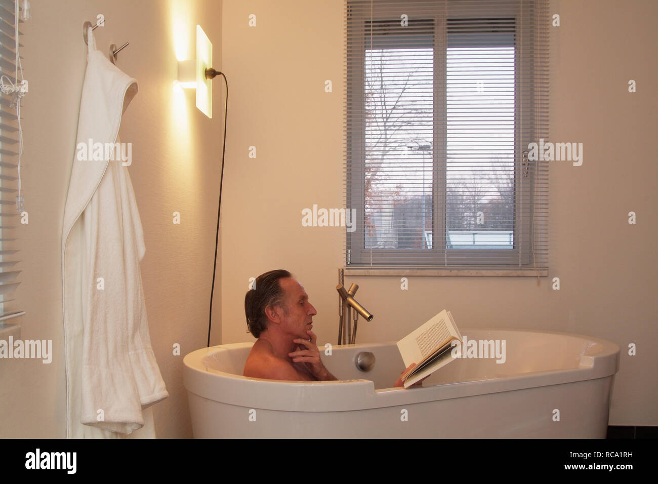 Mann mittleren Alters liest ein Buch in der Badewanne  | middleaged man is reading a book in a bathtub Stock Photo