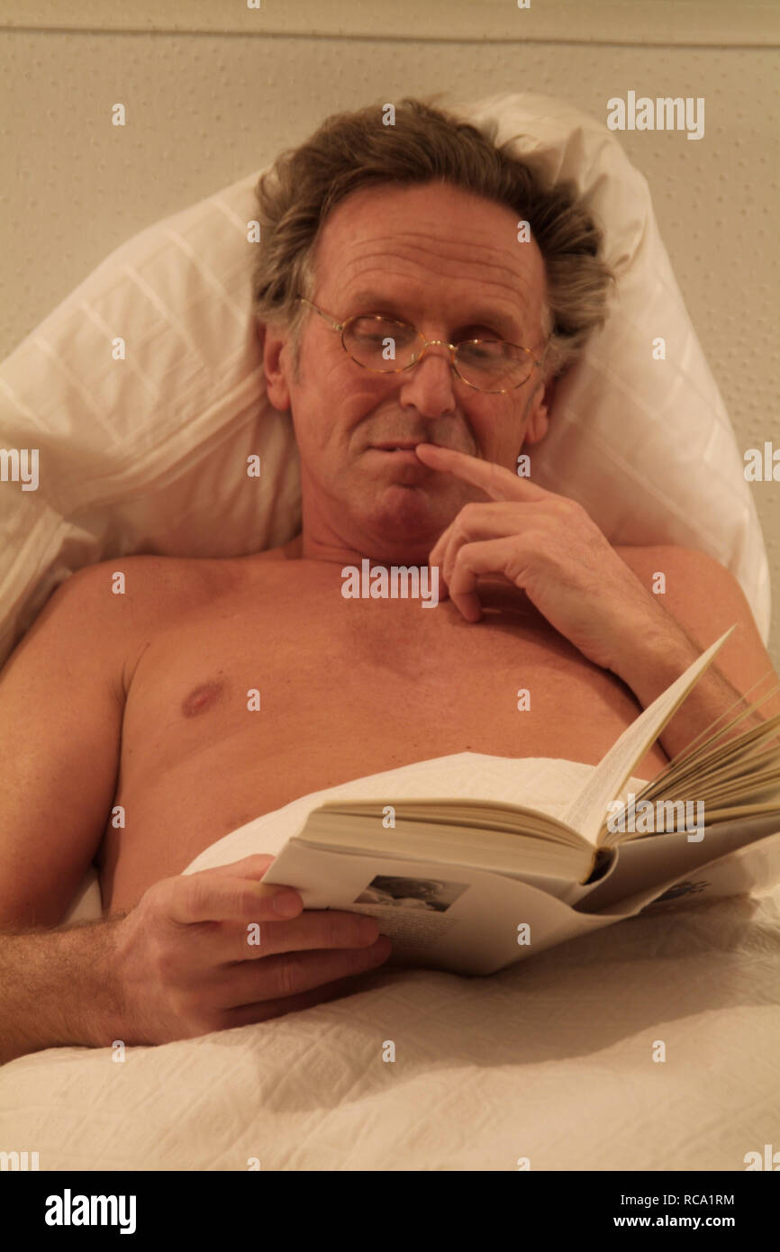 Mann mittleren Alters liest ein Buch im Bett | middleaged man is reading a book in bed Stock Photo