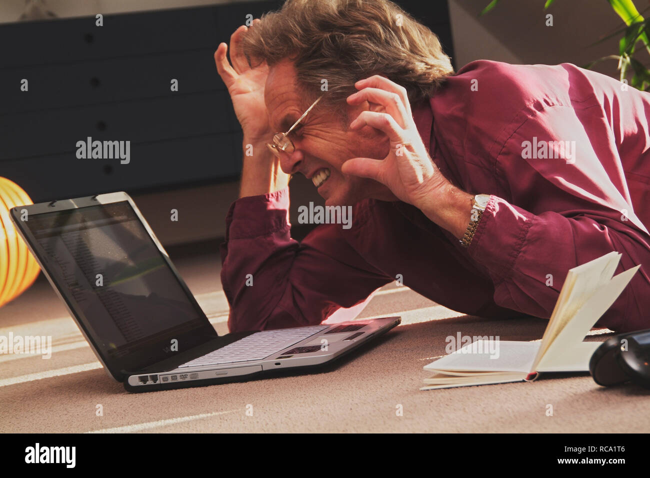 Mann mittleren Alters mit Notebook auf dem Boden liegend ärgert sich | stressed middleaged man is lying on the floor with a notebook Stock Photo