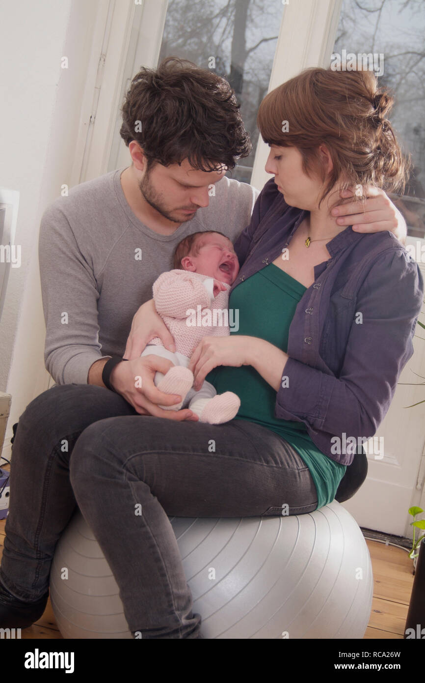 Junge Eltern halten ihre neugeborene Tochter im Arm, das Kind ist 12 Tage alt und schreit | young parents holding her new born baby in her arms - the Stock Photo