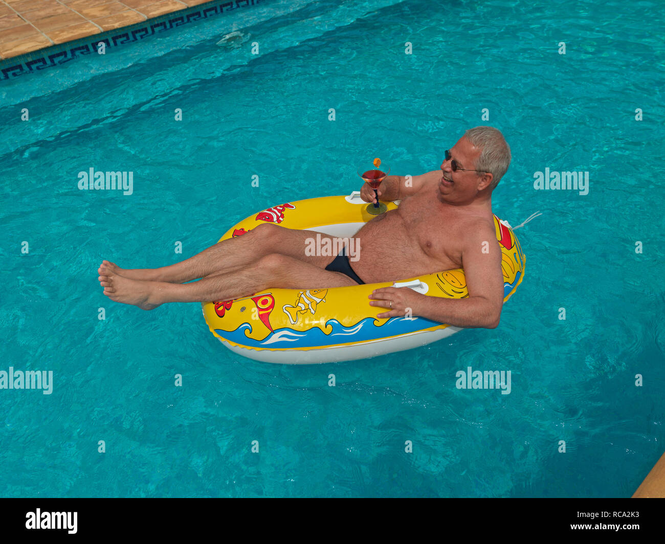 älterer Mann genießt das Leben im kleinen Schlauchboot im Swimmingpool | elderly man with a rubber dinghy in the swimming-pool Stock Photo