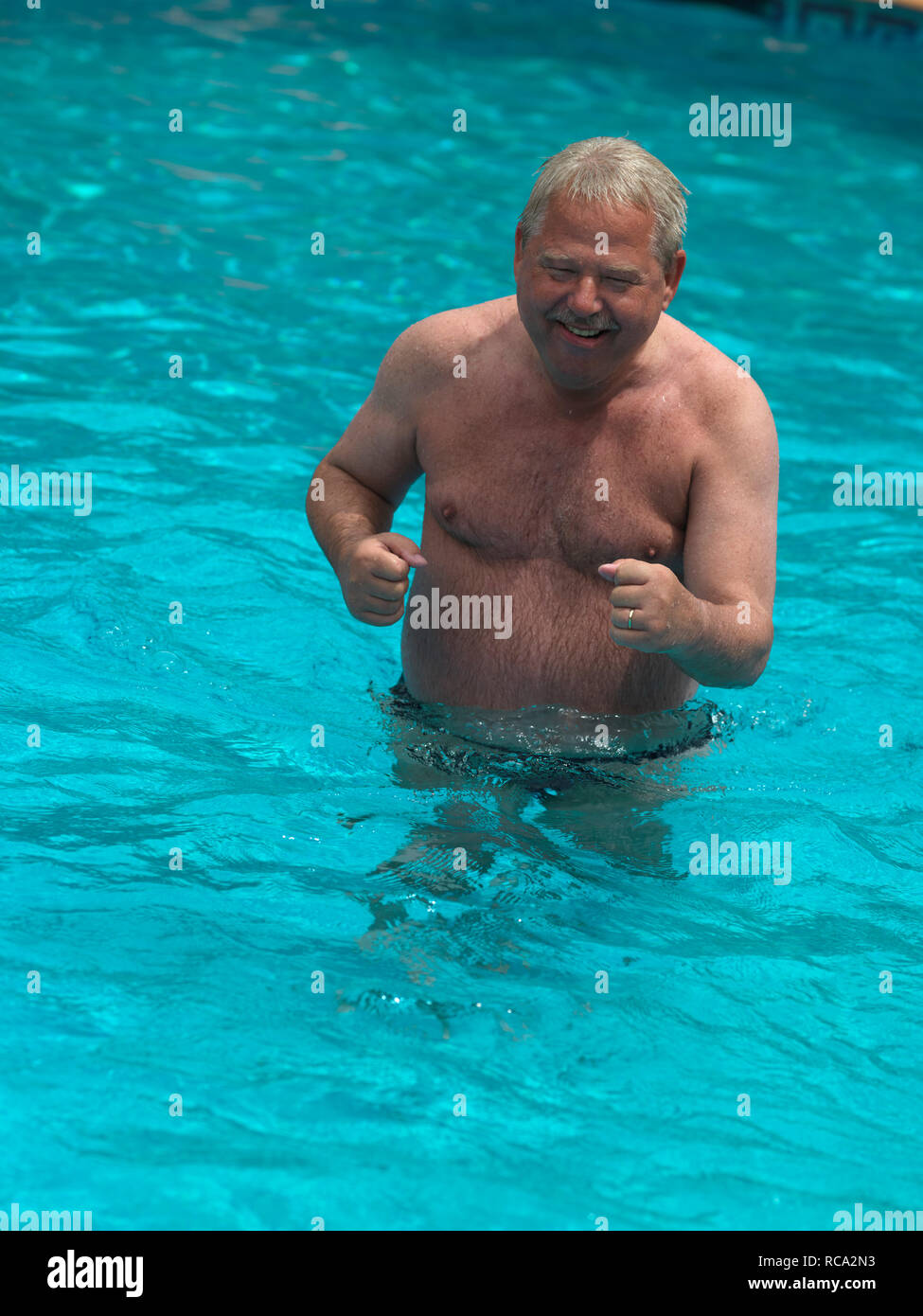 älterer Mann im Swimmingpool macht Wassergymnastik | elderly man smoking in a swimming-pool making water exercises Stock Photo