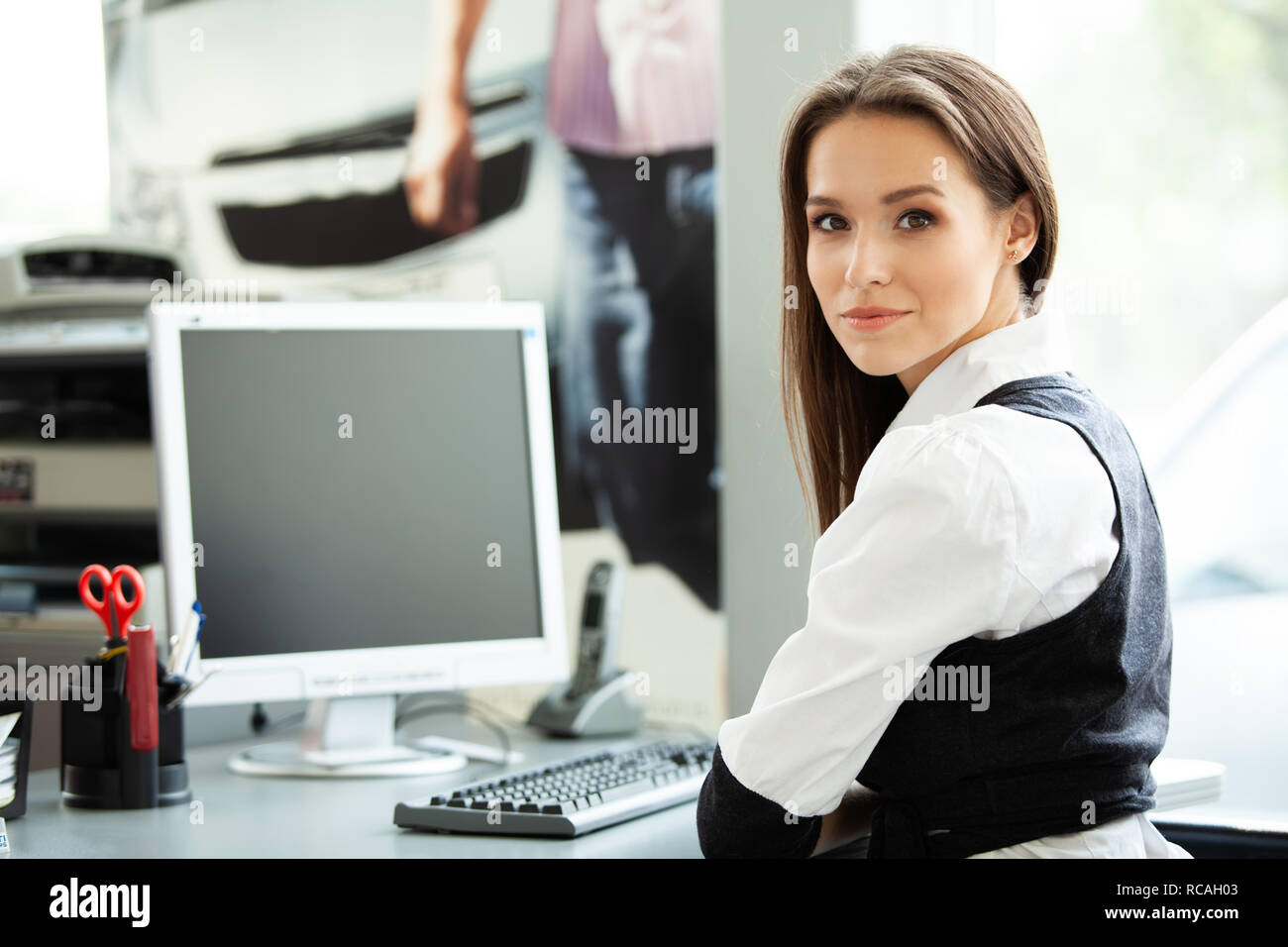 Portrait of smiling pretty young business woman sitting on workplace ...