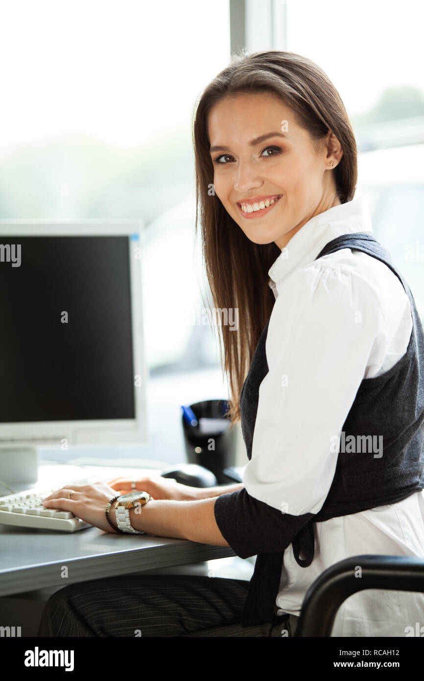 Portrait of smiling pretty young business woman sitting on workplace ...