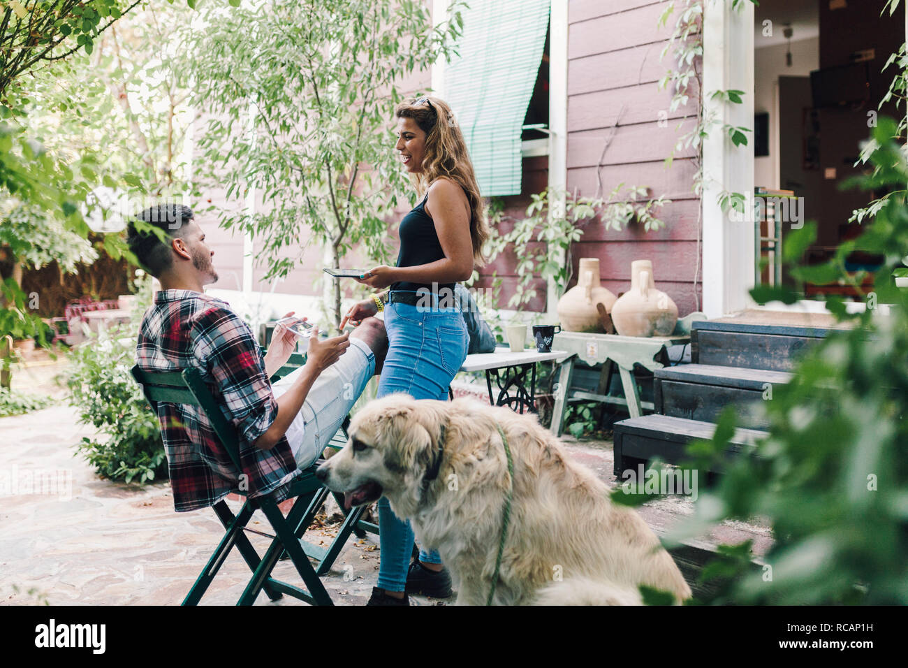 Young couple and their dog sitting smiling in the garden chairs near