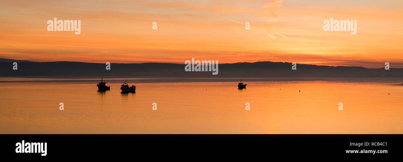 The last of the sunset creating some wonderfully warm and vibrant colours on Holy Island silhouetting the fishing boats and landscape beautifully. Stock Photo