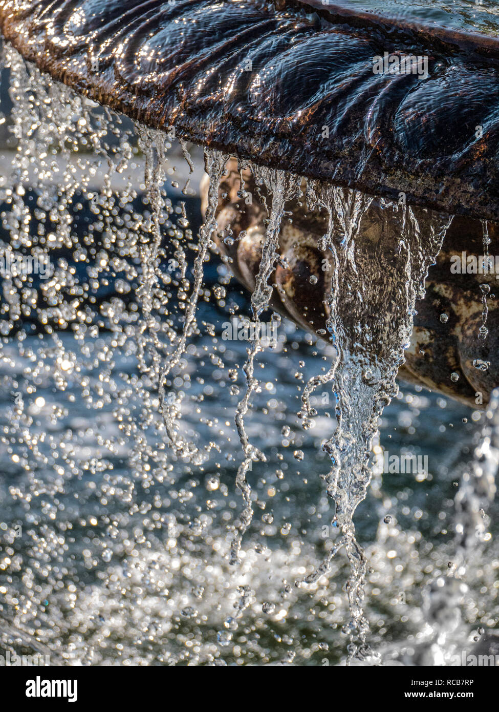 WATER FOUNTAIN DROPS DROPLETS Water flowing off an ornamental old weathered limestone garden feature water fountain in bright sunlit situation Stock Photo