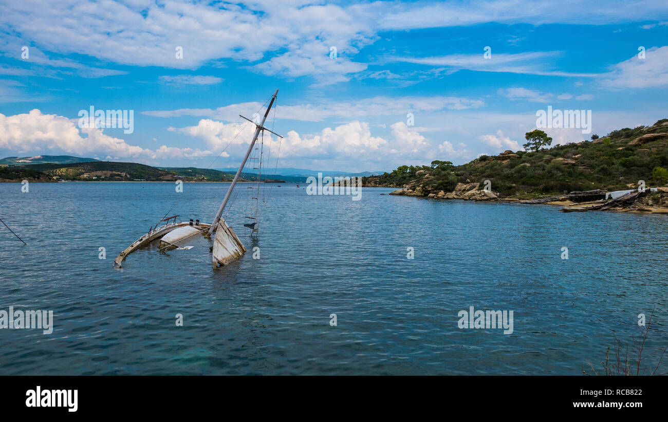 Shipwrecked half-submerged yacht in a calm waters bay at a beautiful exotic location in Greece Stock Photo