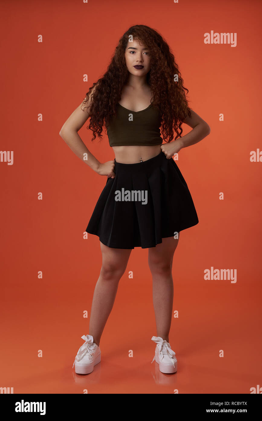 Young woman in skirt standing on orange color studio background Stock Photo