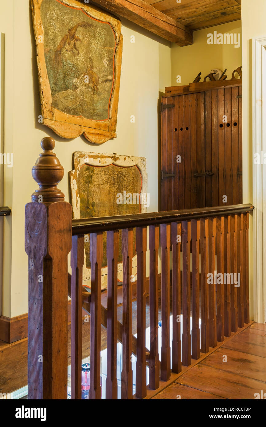 Wall decorated with painted antique carousel wood panels and wooden newel post and railing on upstairs floor hallway inside old 1835 fieldstone home. Stock Photo