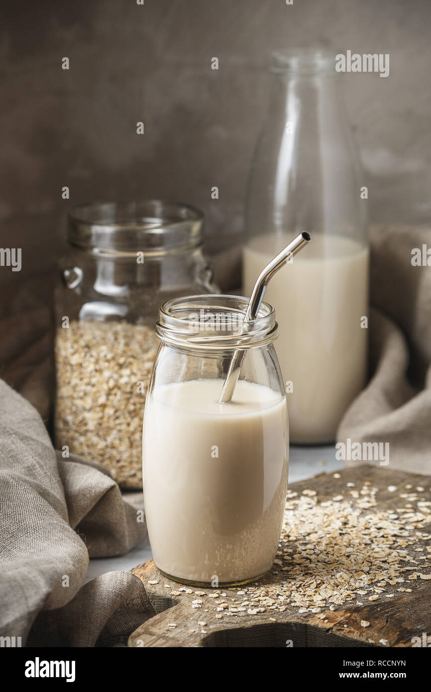 Non dairy oat milk in glass jar with metal reusable drinking straw on rustic background. Oat flakes scattered on the table. Stock Photo