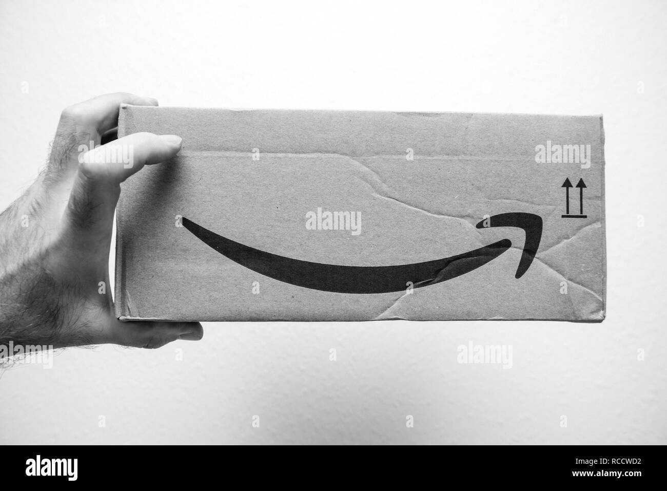 PARIS, FRANCE - JAN 6, 2018: Hand holding cardboard box with Amazon Logotype Smile logo arrow - black and white image  Stock Photo