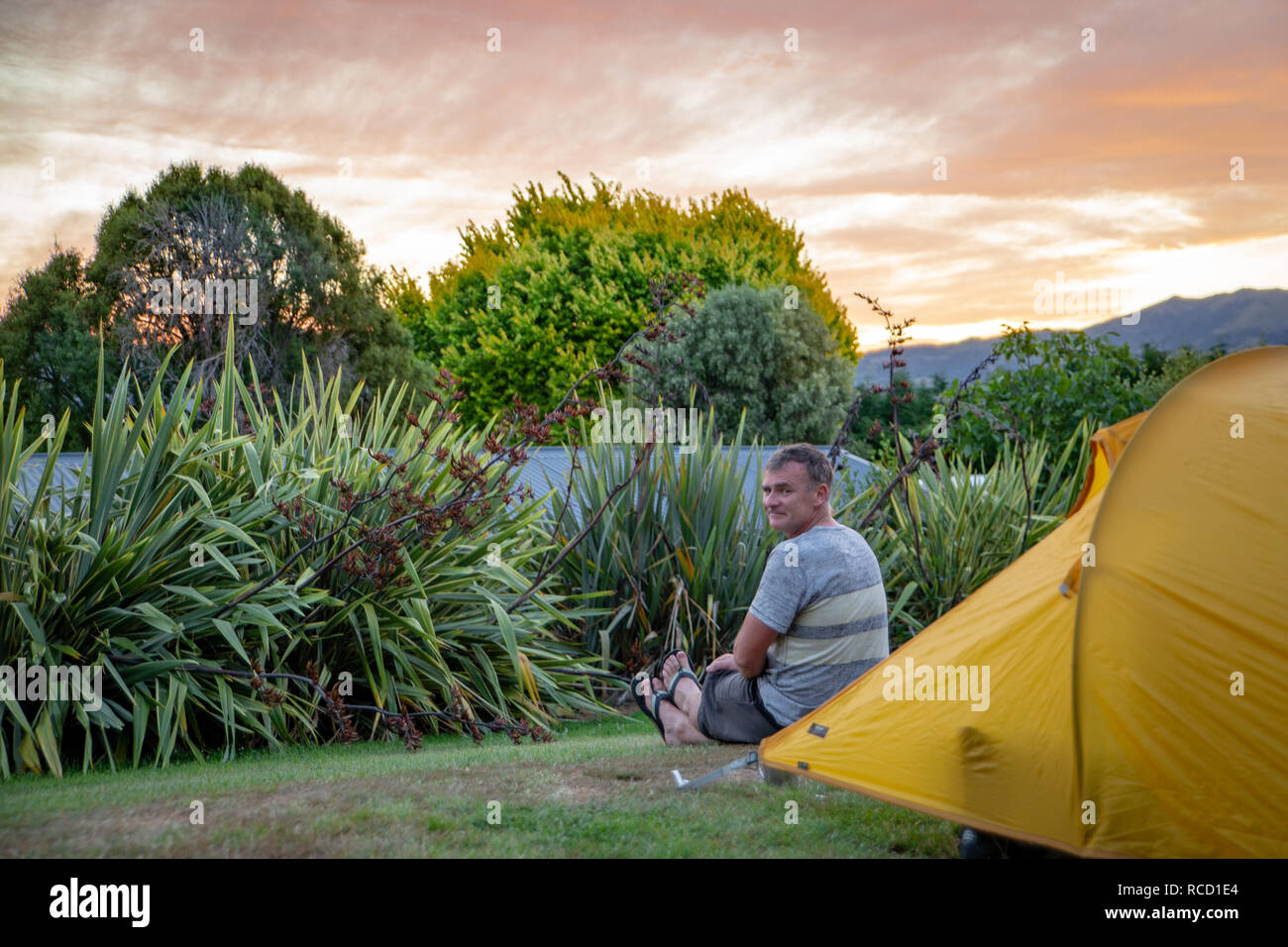 A tourist enjoys the evening sunset outside his tent at the holiday park in Akaroa, New Zealand Stock Photo