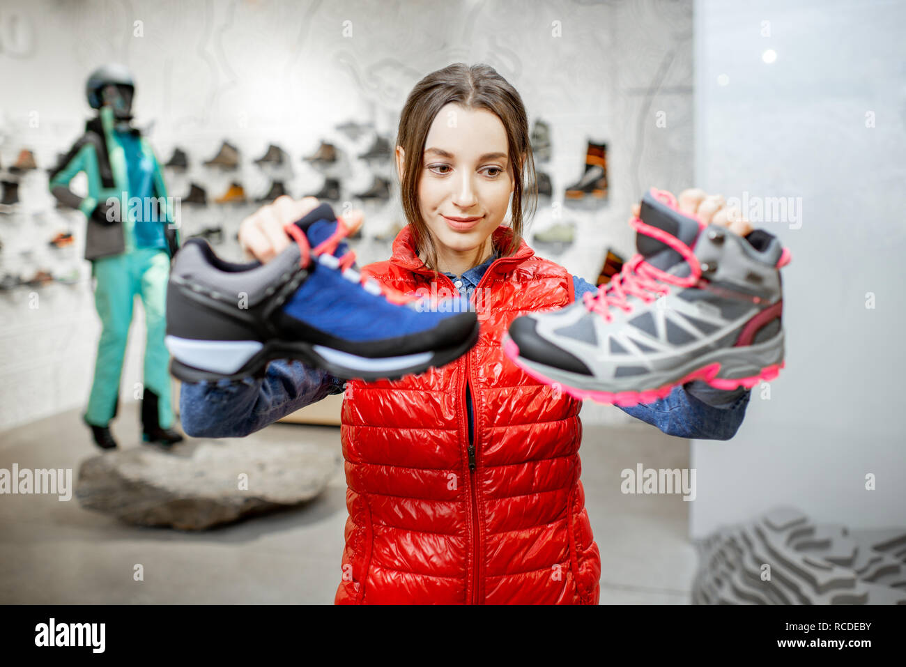 Young woman choosing trail shoes for mountain hiking in the modern sports shop Stock Photo