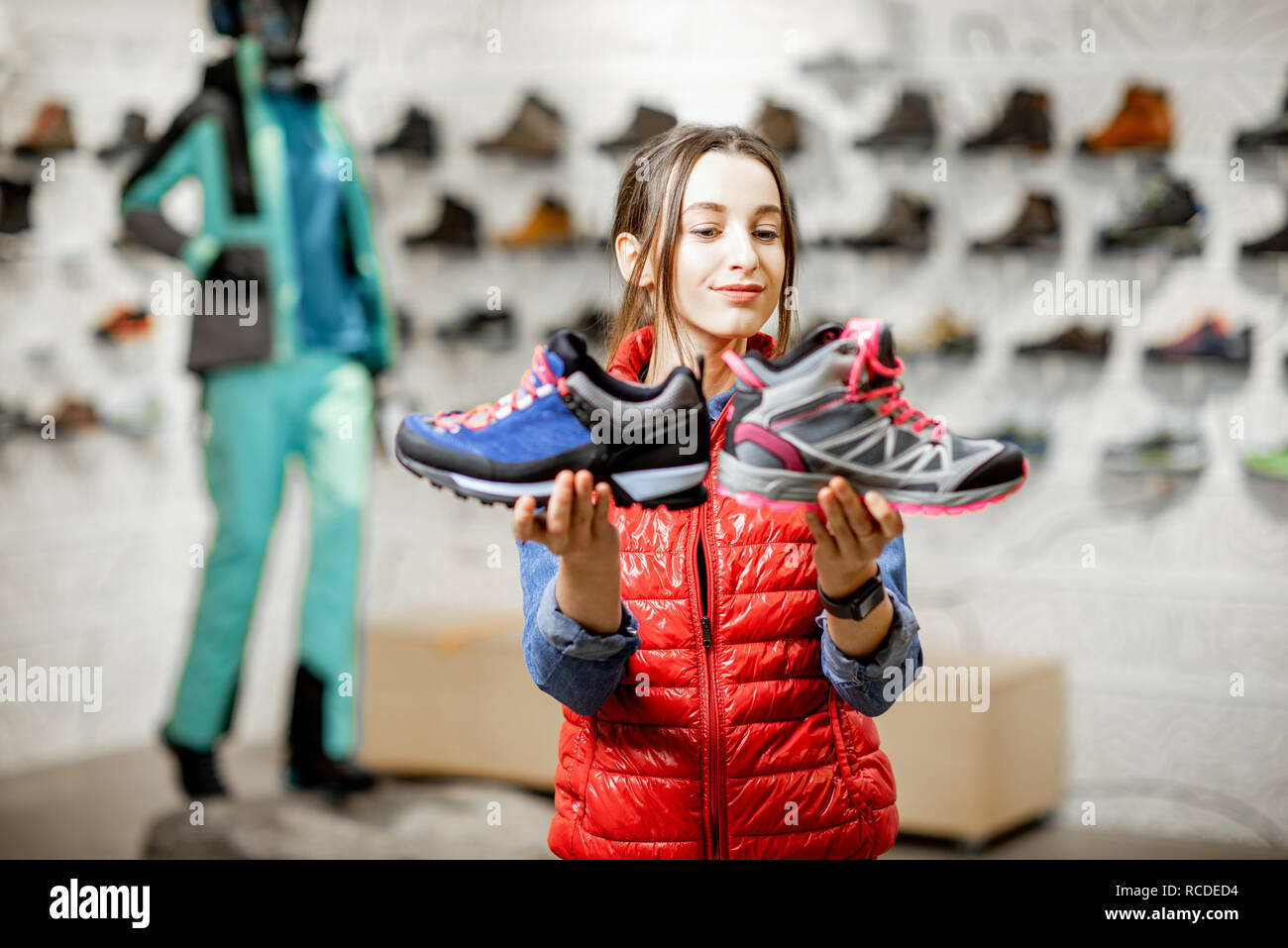 Young woman choosing trail shoes for mountain hiking in the modern sports shop Stock Photo