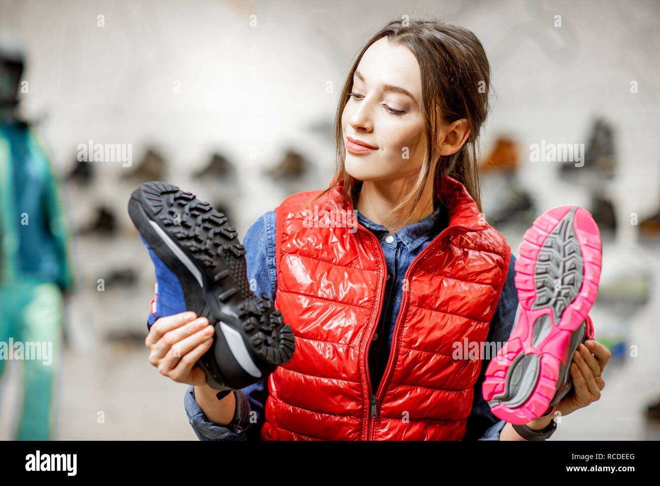 Young woman choosing trail shoes for mountain hiking in the modern sports shop Stock Photo