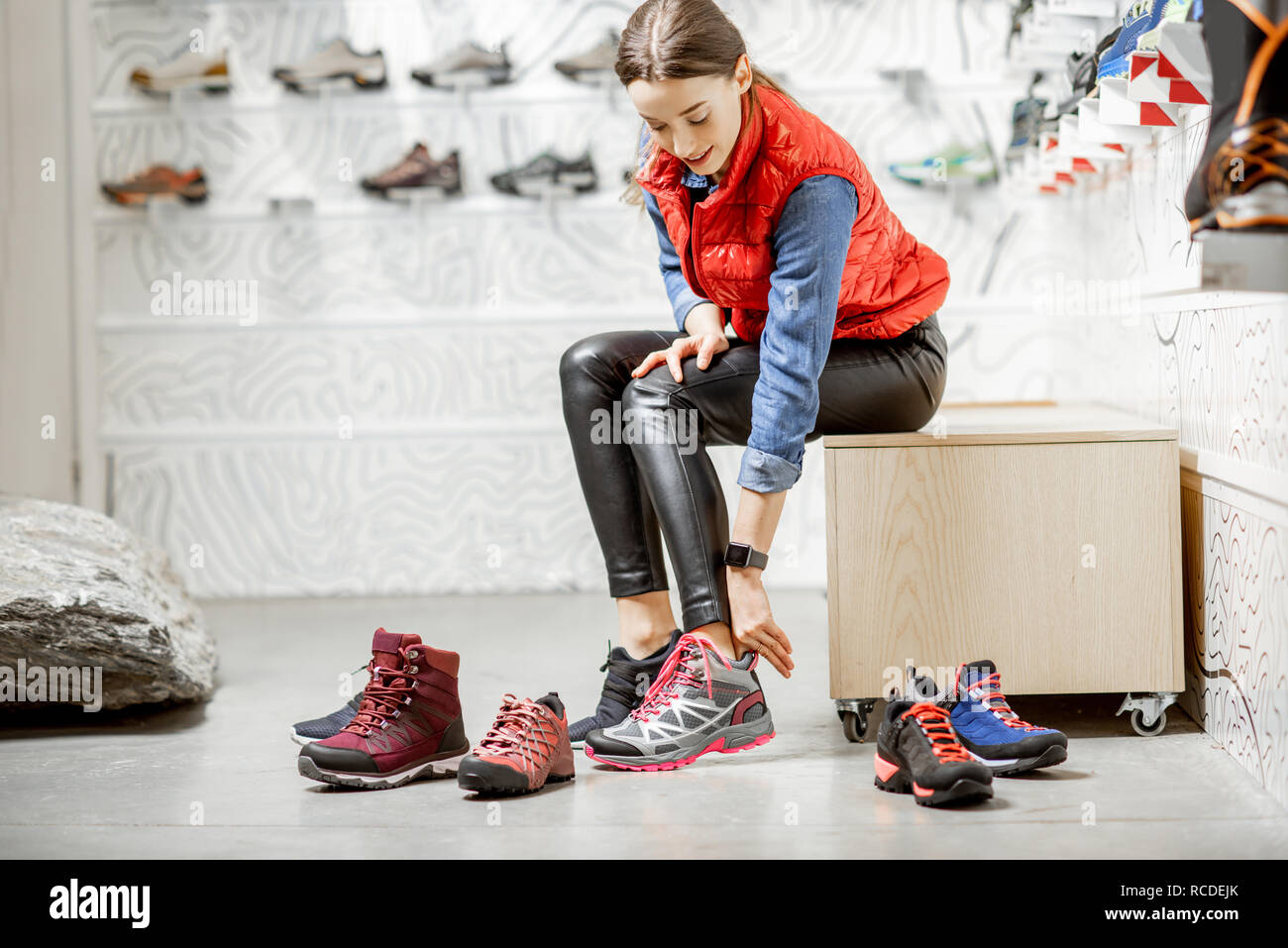 Woman trying shoes for mountain hiking sitting in the fitting room of the modern sports shop Stock Photo